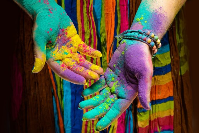 Multi-colored hands in front of vibrantly colored garment.